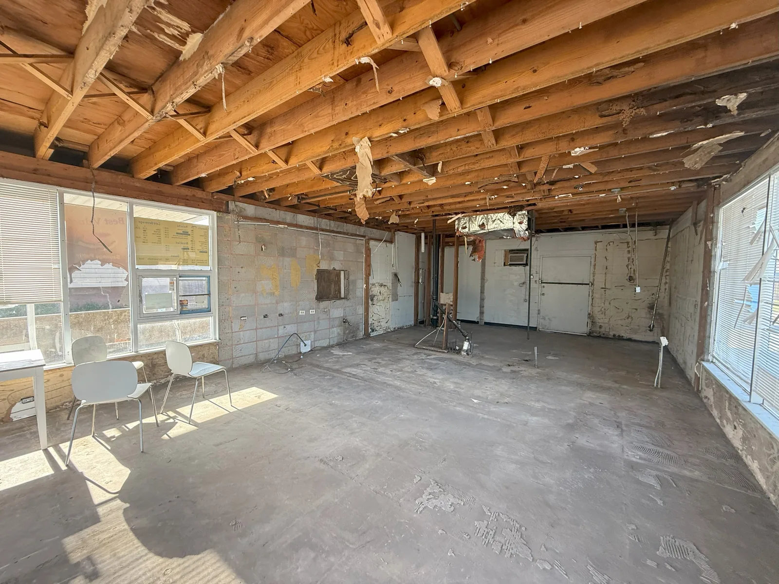 The gutted shell after demolition, stripped back to bare joists and block walls, with the original menu board still hanging in the window.